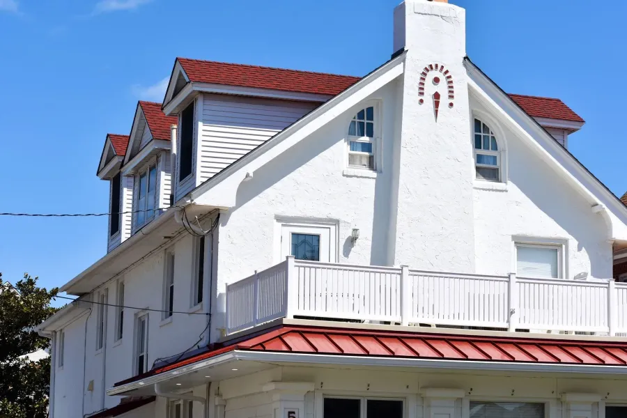 White stucco home with red metal roof and white balcony railing in Ventnor, NJ